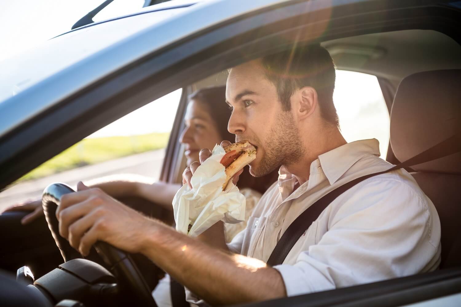 Ein Paar sitzt im Auto und der Mann isst während der Fahrt ein Baguette
