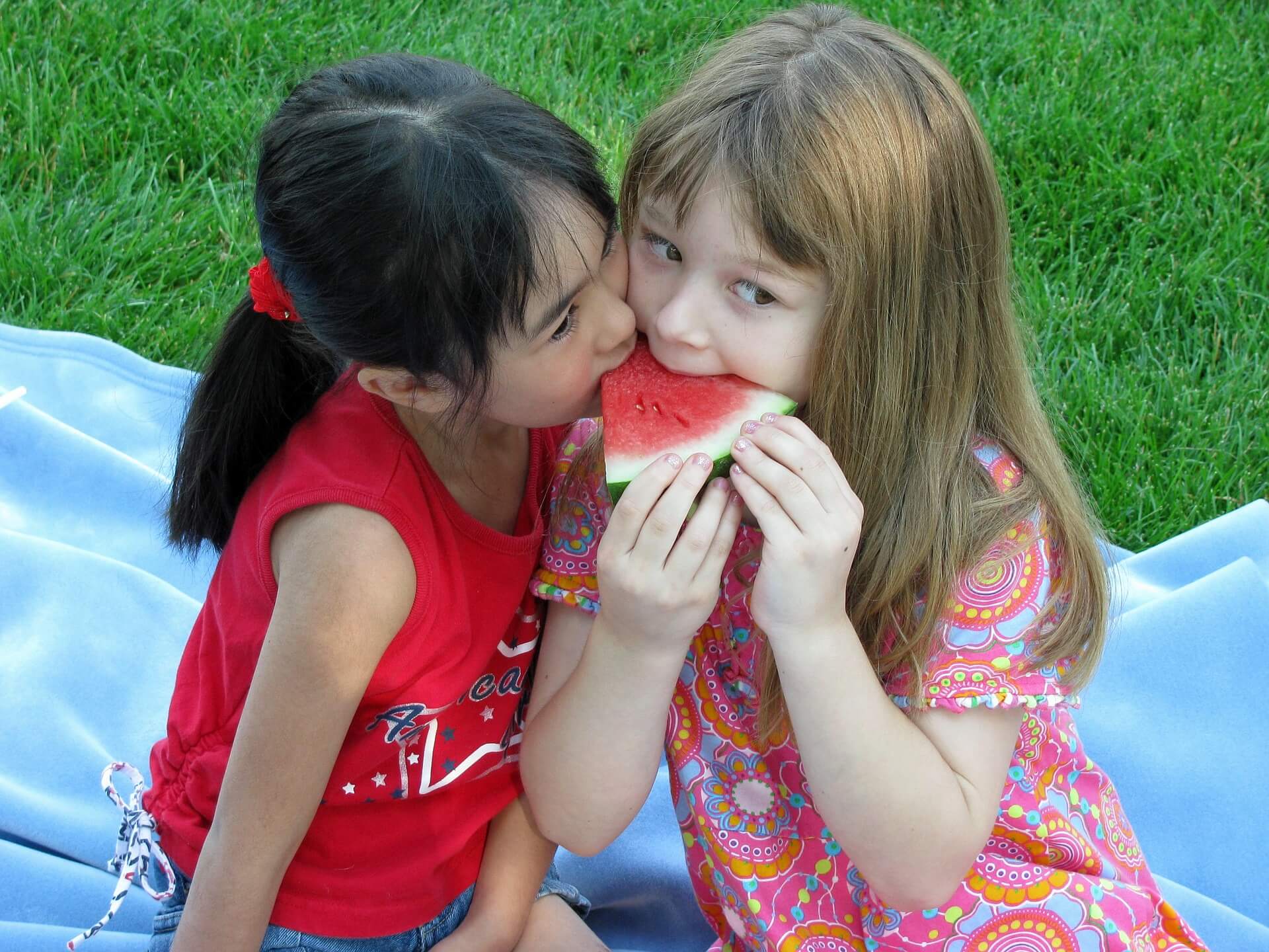 Zwei kleine Mädchen essen ein Stück Wassermelone. Wenn man die Melonenstücke über Nacht in die Gefriertruhe legt, hat man ein selbst gemachtes, einfaches Melonen-Eis.