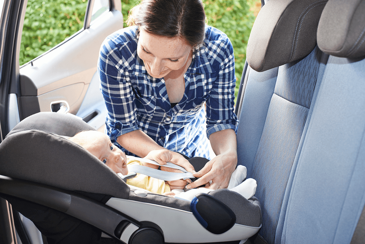Mama schnallt Baby im Reboarder-Kindersitz im Auto an