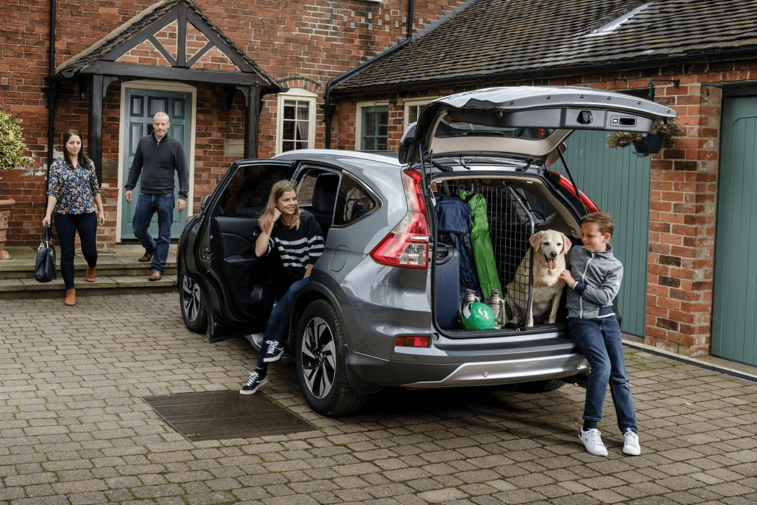 Für den Urlaub mit Hund hat sich die Familie im Foto entschieden, den Hund mit Hundegitter und Kofferraumteiler von Travall im Auto zu sichern. © Travall