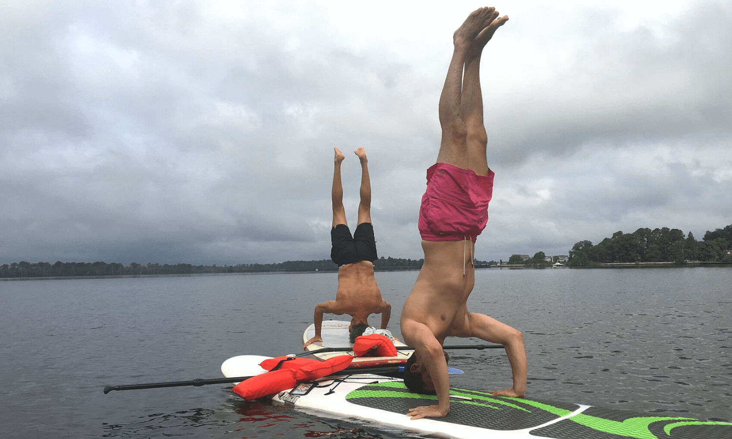 Um die Fitness zu steigern und mehr Motivation für Sport zu bekommen, muss man die richtige Sportart finden. Auf dem Foto machen zwei Männer Yoga auf einem SUP Brett. Sie üben Handstand. © iStock.com