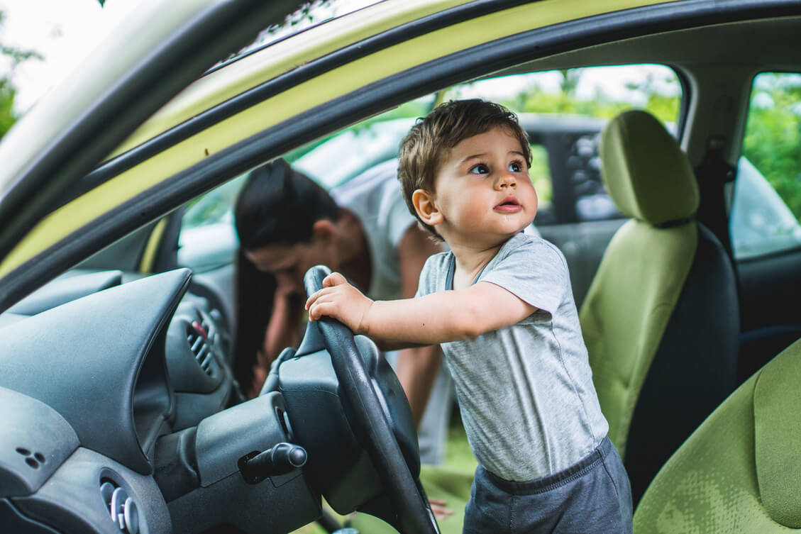 A child standing on a driver's seat pretending to drive a car. 