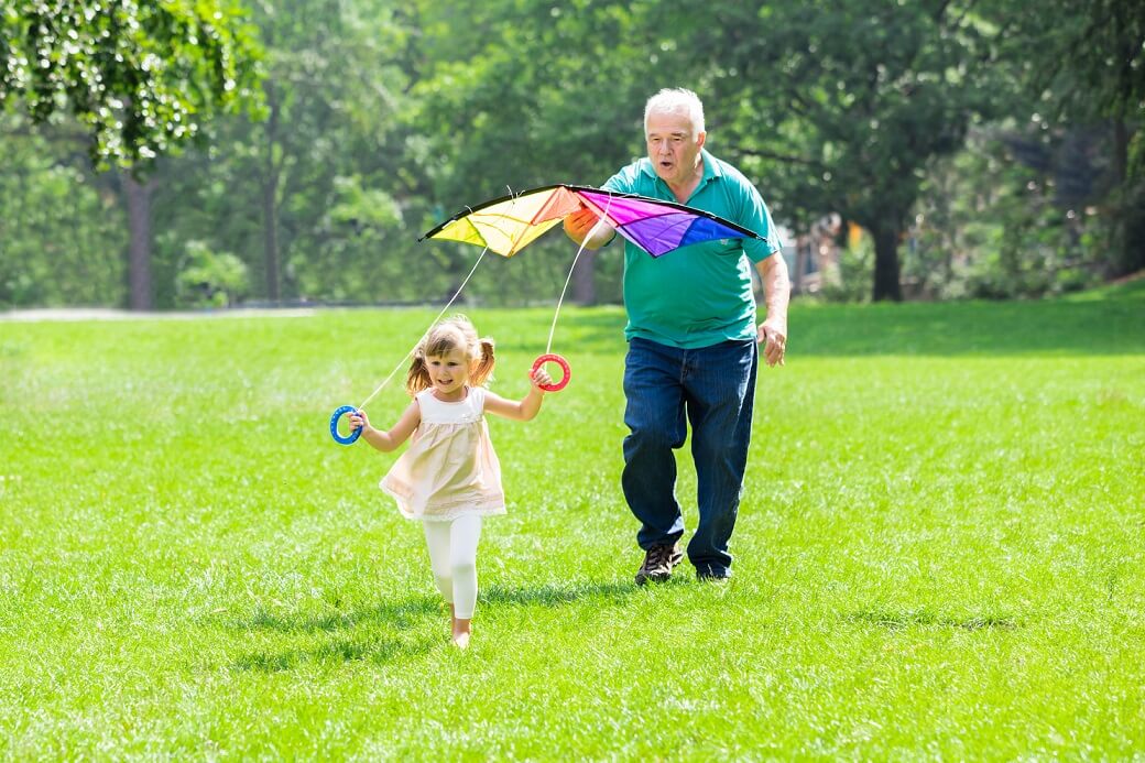 Grandfather Helping Kid To Fly Kite In Park