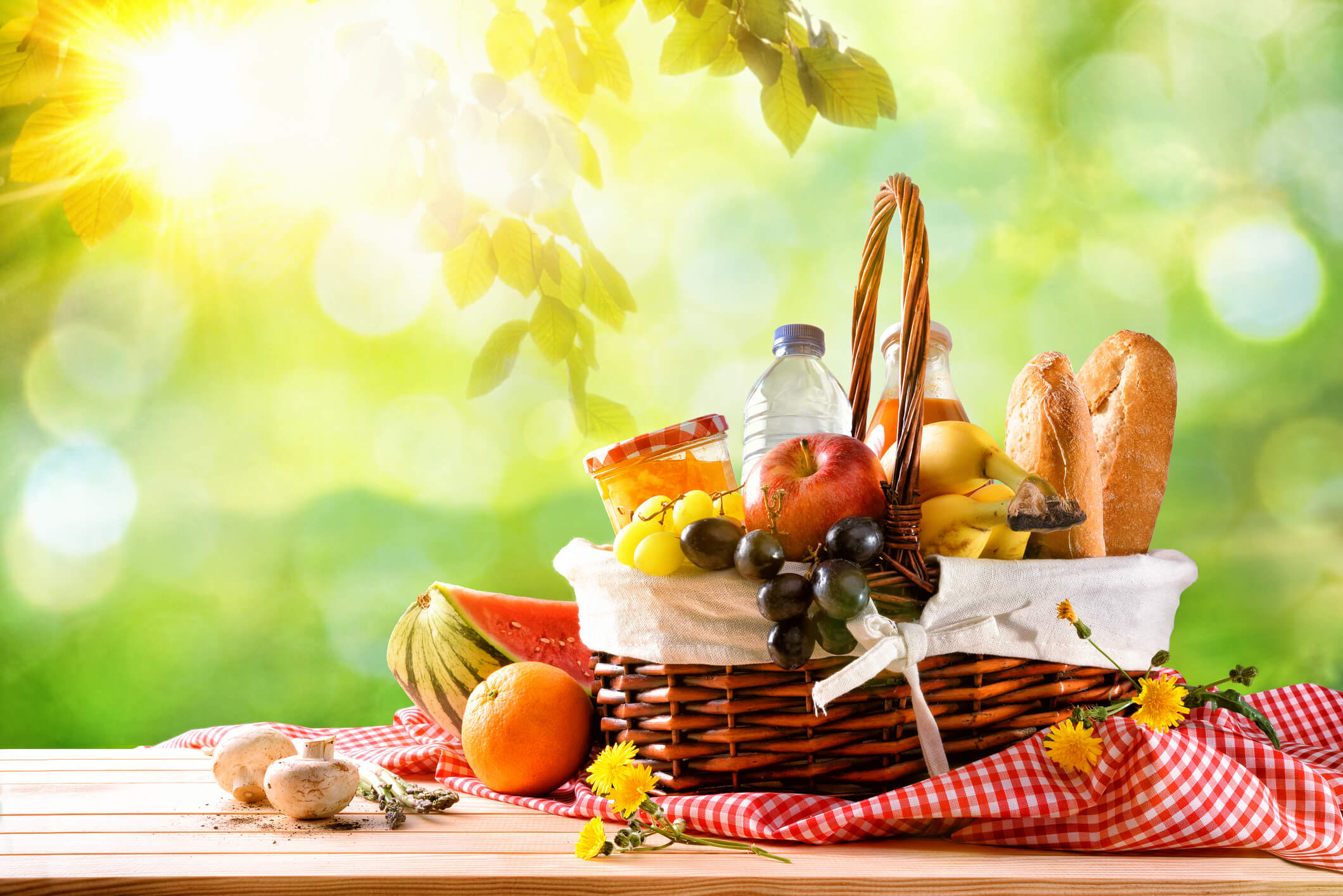 Picnic wicker basket with food on table in the field with green nature background. 